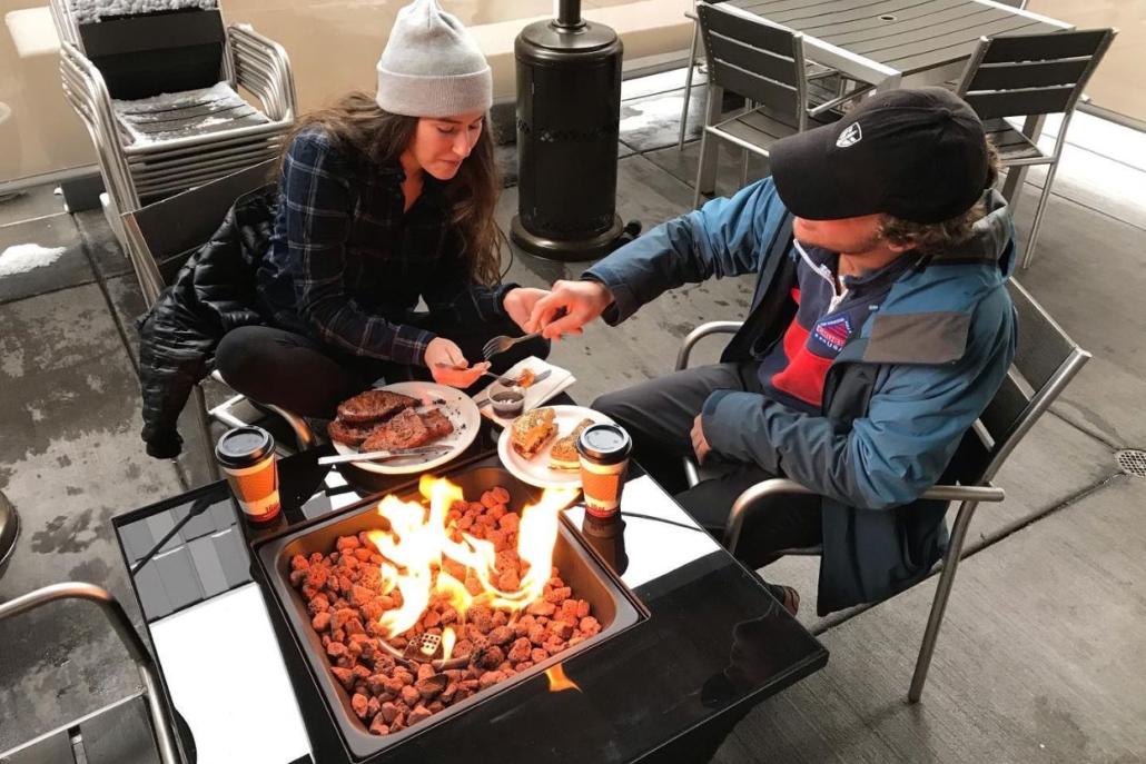 The couple enjoying a meal together around a fire pit at an Aspen coffee shop, creating a warm and relaxing setting.