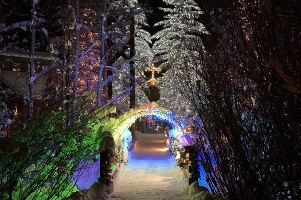 A charming Christmas scene in Aspen, Colorado, showcasing a lighted archway along a walkway surrounded by trees.