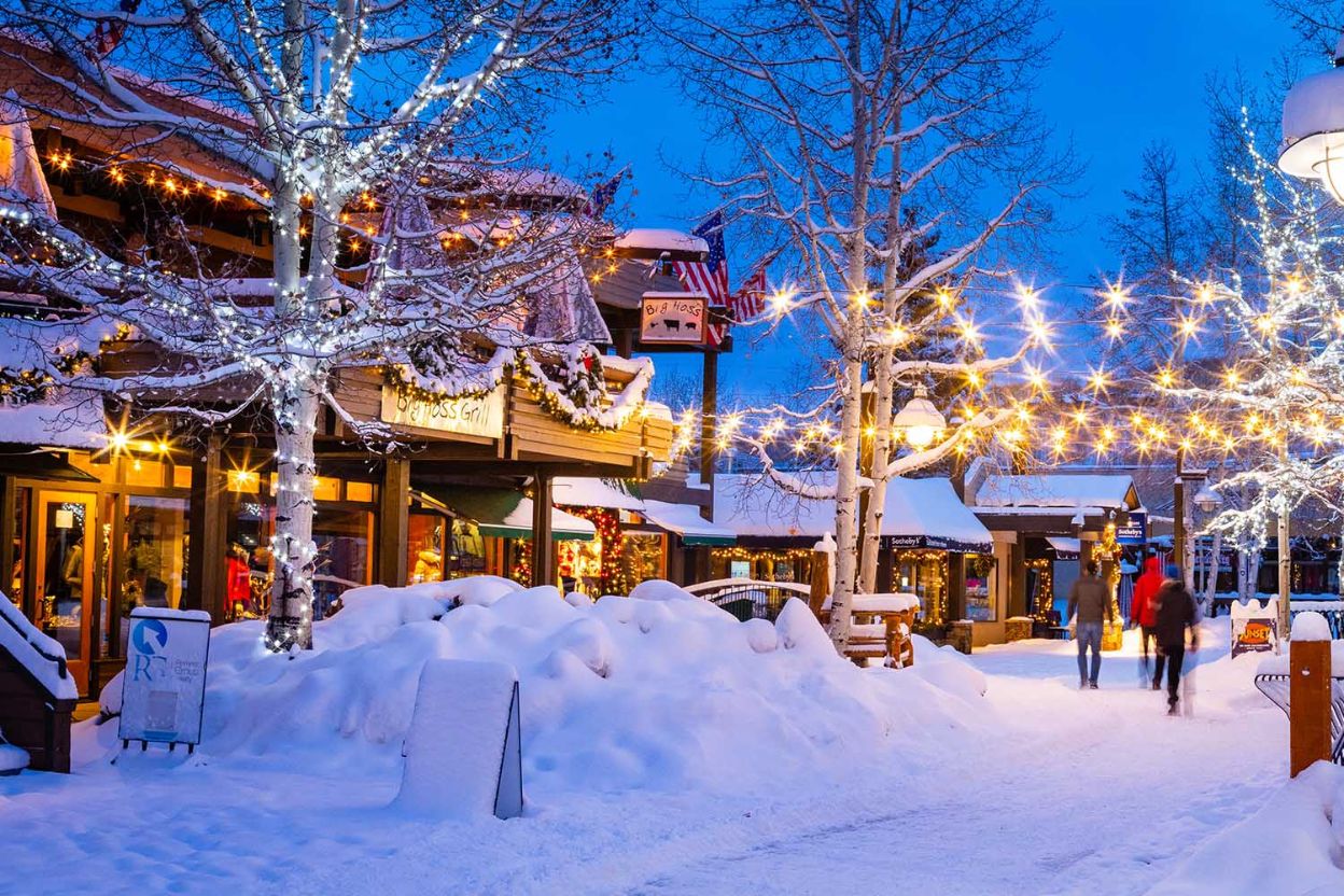 A snowy street in Aspen, Colorado, adorned with festive lights and people strolling joyfully during the Christmas season.