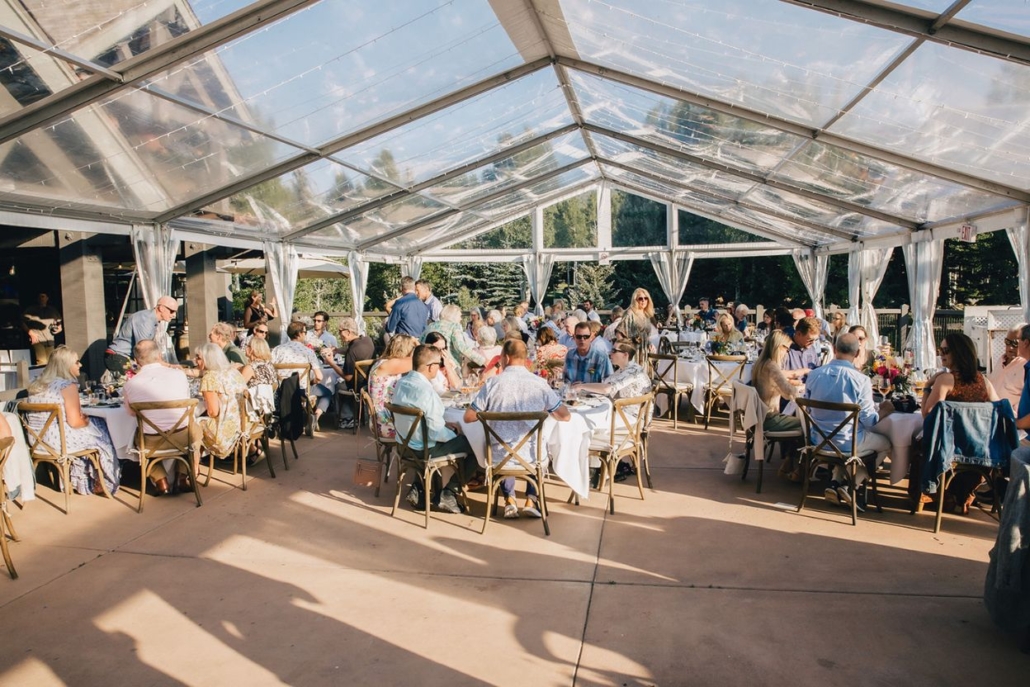 Guests gather at tables under a spacious tent for a wedding reception, celebrating with joy and culinary delights in Aspen.