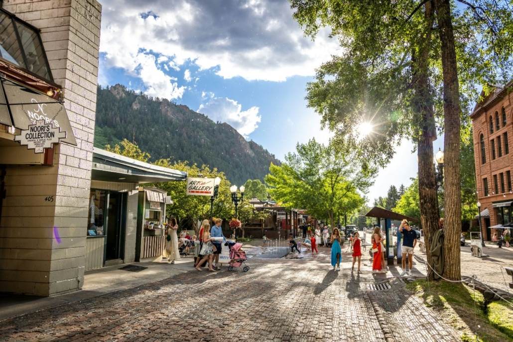 A bustling scene of people strolling along a brick street in downtown Aspen, surrounded by charming shops and cafes.