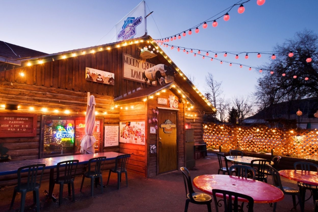 Outdoor dining area of Woody Creek Tavern, featuring tables and chairs illuminated by soft lights under the night sky.