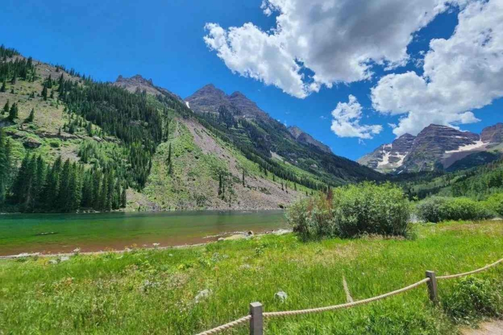 Scenic mountain lake in Aspen surrounded by lush greenery and dramatic peaks under a bright blue sky