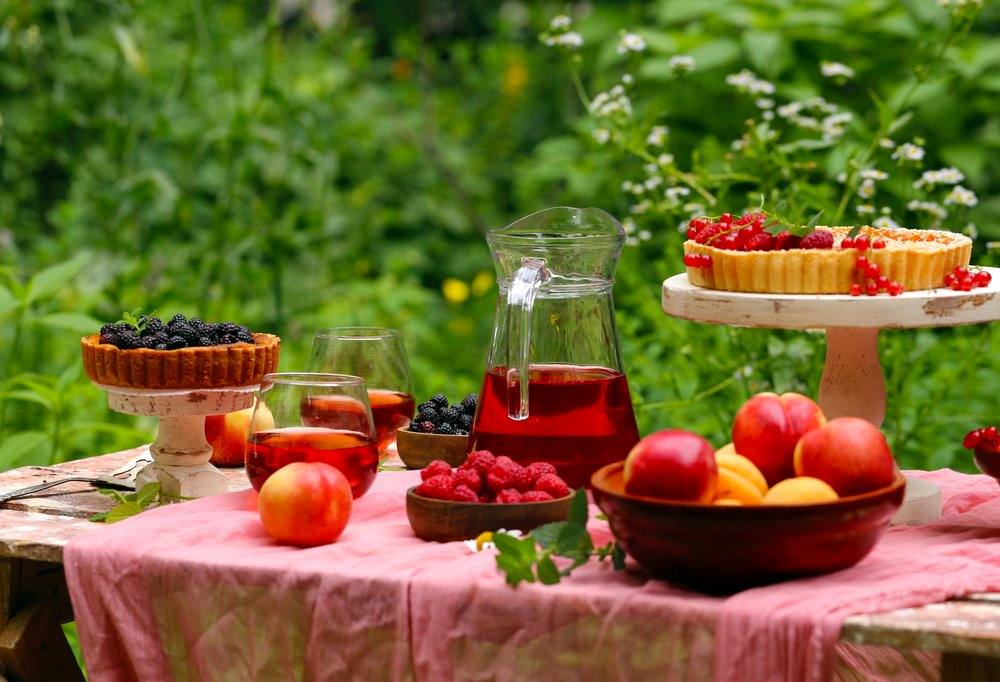 Elegant outdoor picnic setup with fruit tarts, fresh berries, and drinks arranged on a table surrounded by lush greenery