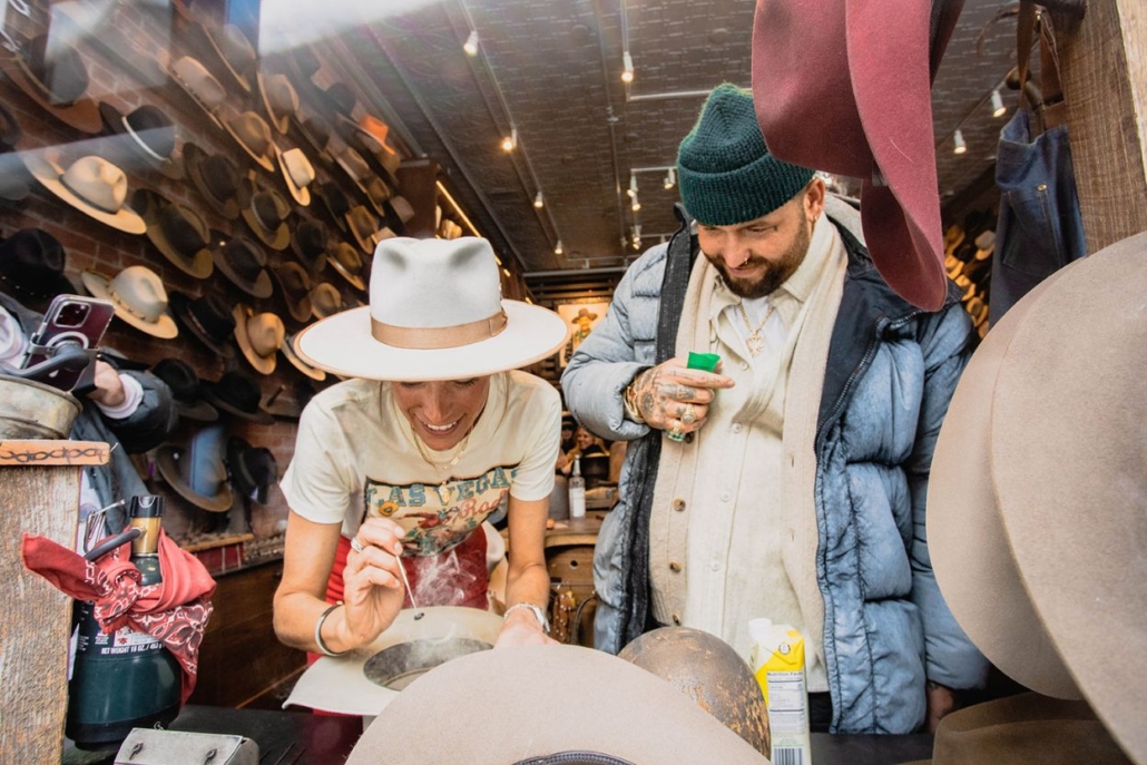 Two individuals browse a selection of hats in a store while shopping in Aspen, surrounded by a vibrant retail atmosphere.