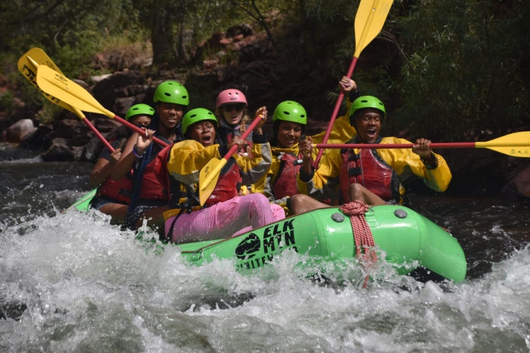 A group of individuals in green and yellow rafts navigating the Roaring Fork River during a water rafting adventure.