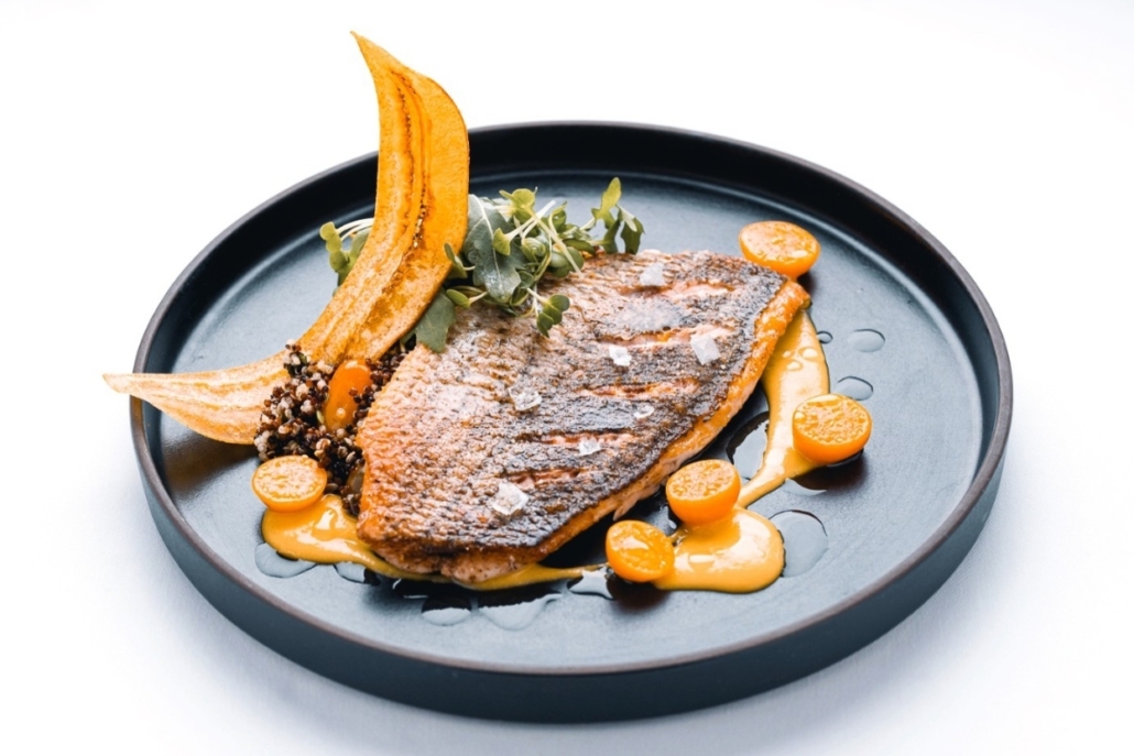 A beautifully presented fish on a plate, complemented by a rich orange sauce, highlighting a gourmet dish.