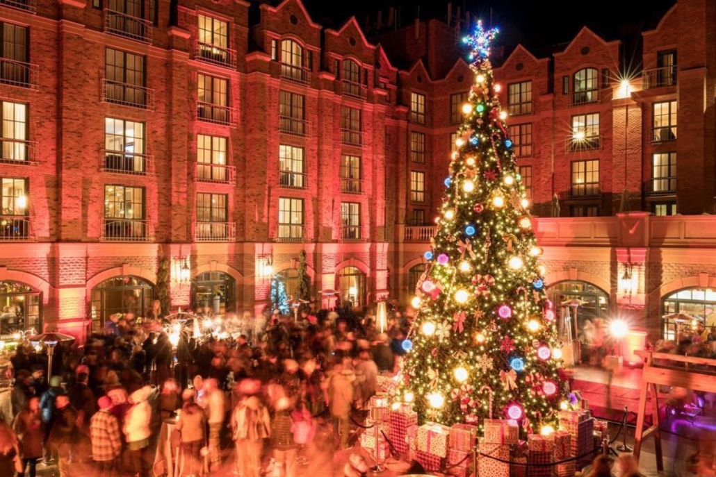 A beautifully lit large Christmas tree stands proudly in the center of a courtyard during the Aspen Christmas Tree Lighting Ceremony.