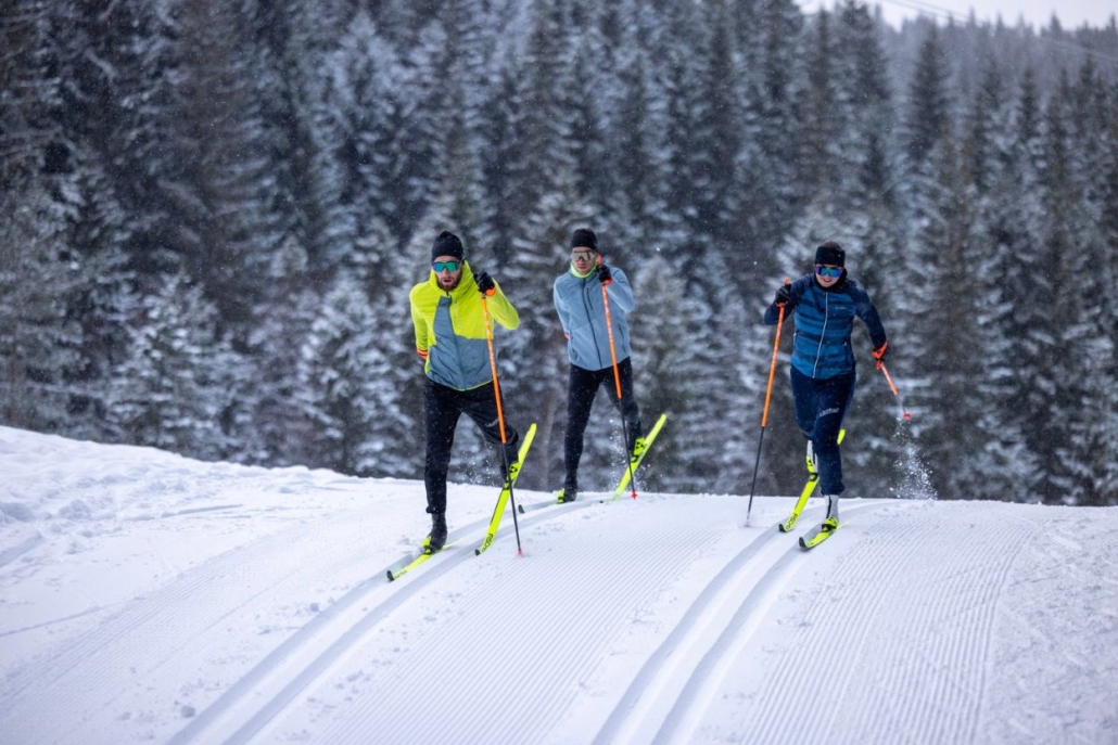 Three individuals cross-country skiing along a snowy trail, surrounded by a serene winter landscape in Aspen in December.