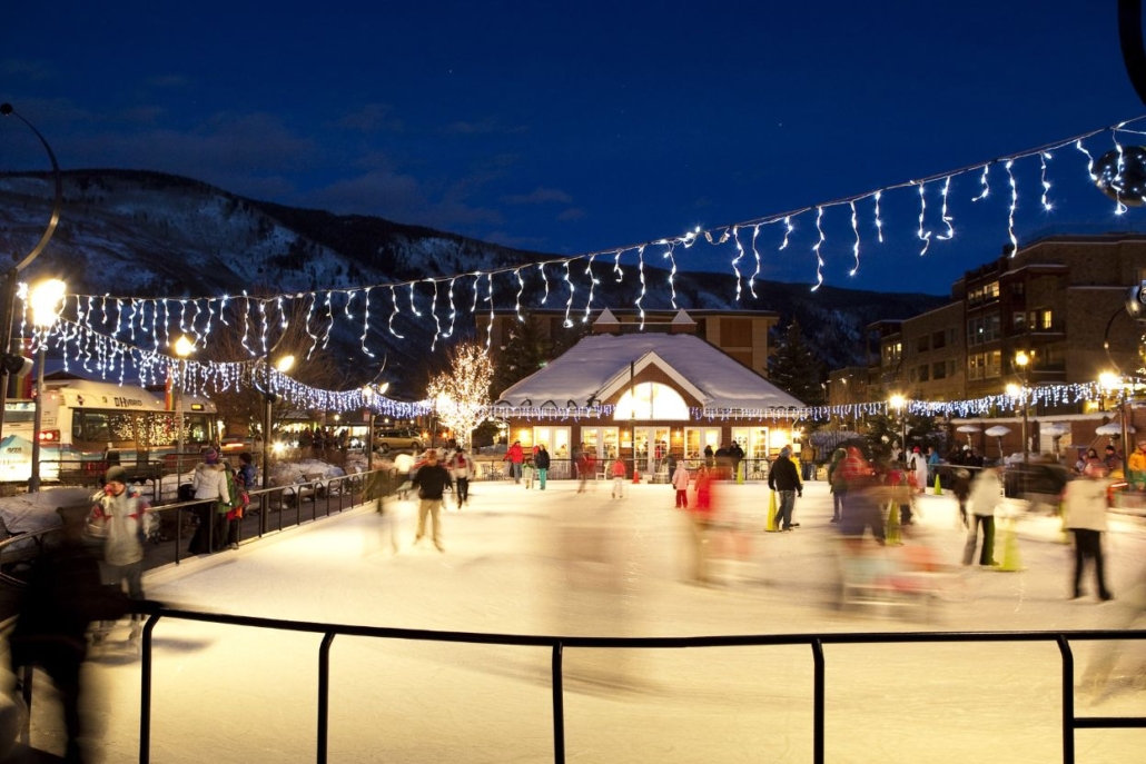 A lively night scene of people joyfully skating on an ice rink in Aspen, surrounded by twinkling lights in December.