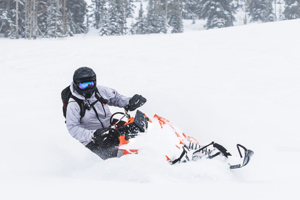 A person rides an orange snowmobile through the snowy landscape of Aspen in December, enjoying the winter adventure.