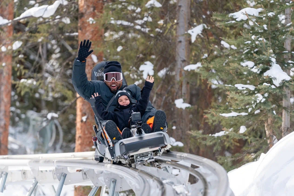 A man and his child joyfully ride a snow tube down a snowy slope, capturing the thrill of winter fun in Aspen.