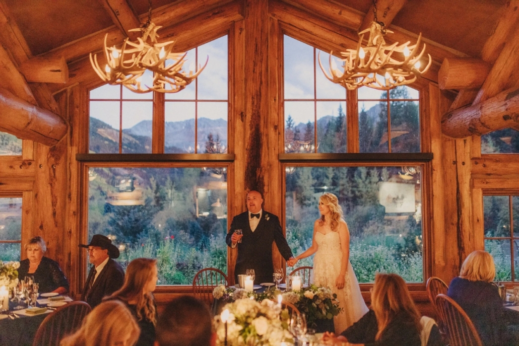 A bride and groom pose in front of the lodge's expansive windows, celebrating their intimate elopement at Pine Creek Cookhouse.