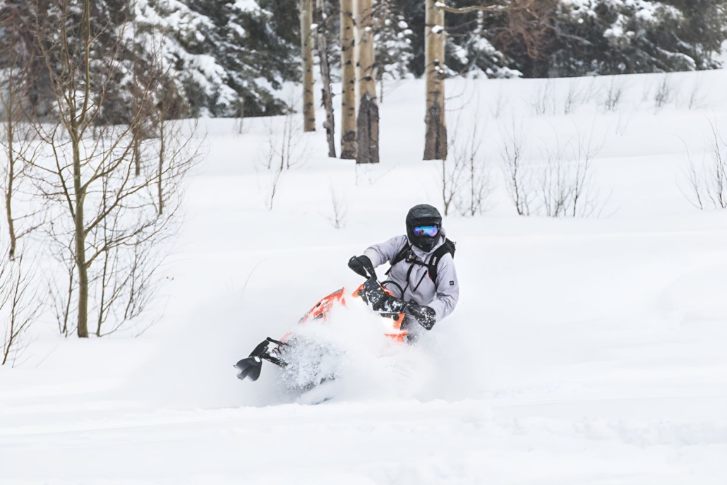 Individual riding an orange snowmobile, navigating through a snowy terrain in Aspen