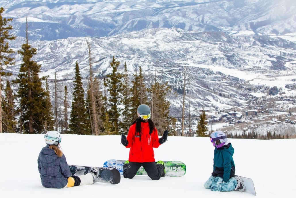 A group of individuals enjoying a snowy landscape, seated together in Snowmass, Aspen, with their snowboard amidst a luxurious winter setting.