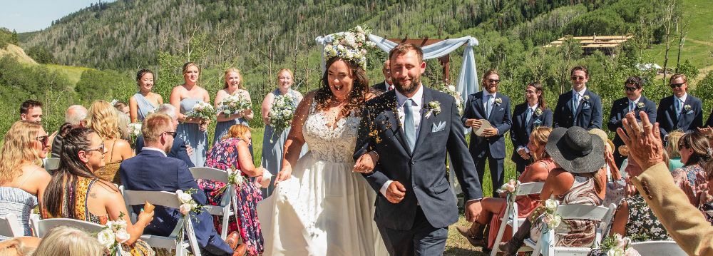 A bride and groom joyfully walk down the aisle at their Aspen wedding ceremony, surrounded by beautiful scenery.