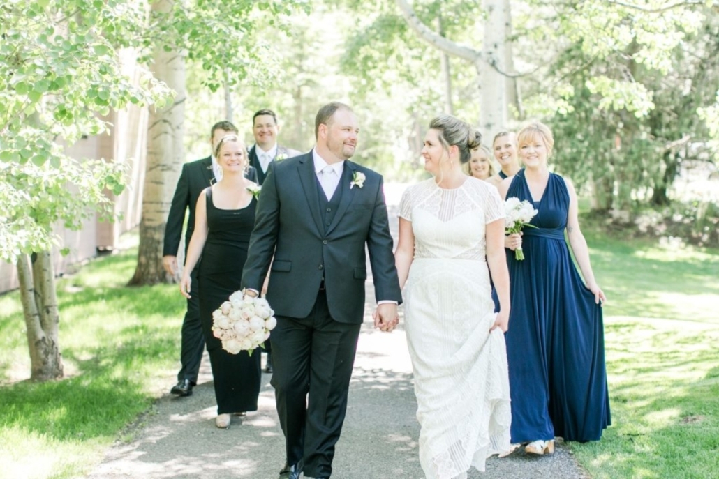 The bride and groom walk joyfully along a path, surrounded by their wedding party in a picturesque Aspen setting.