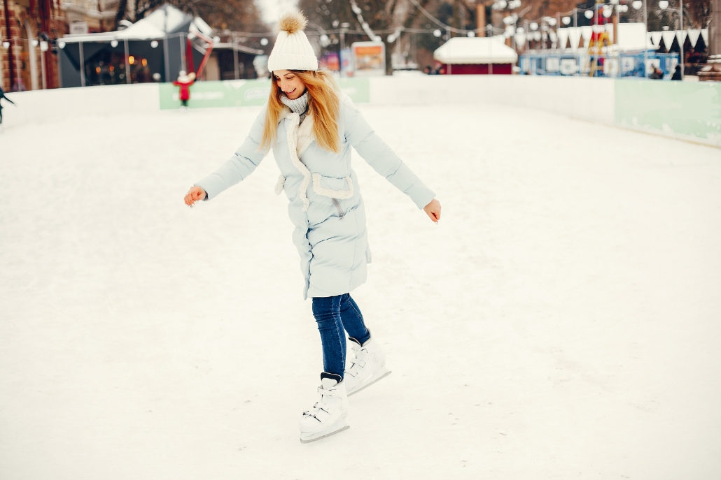 A woman wearing a coat and white hat glides on an ice rink in Aspen, surrounded by a winter landscape in December.