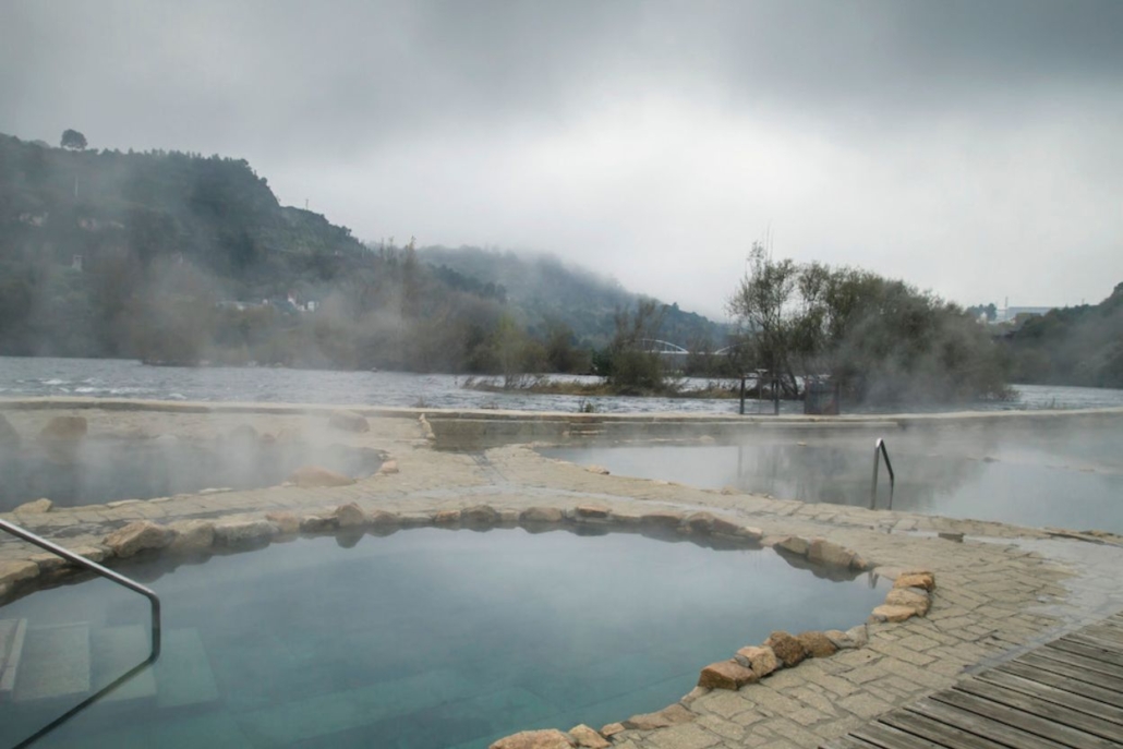 A serene hot spring surrounded by a lake, featuring a wooden walkway leading to the aspen hot springs.