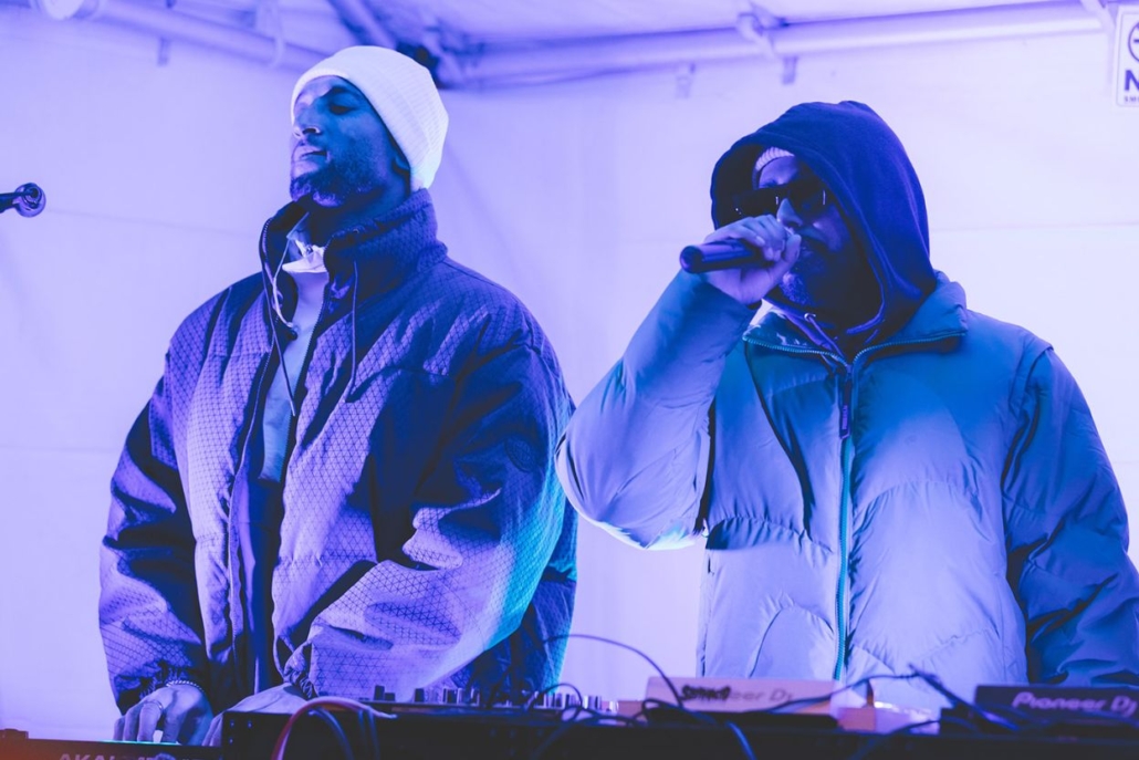 Two men stand side by side on stage, engaging the audience at an Aspen DJ event.