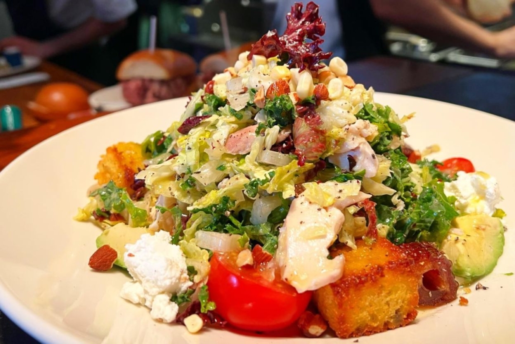 A vibrant salad featuring fresh vegetables and meat, elegantly presented on a white plate at The White House Tavern.