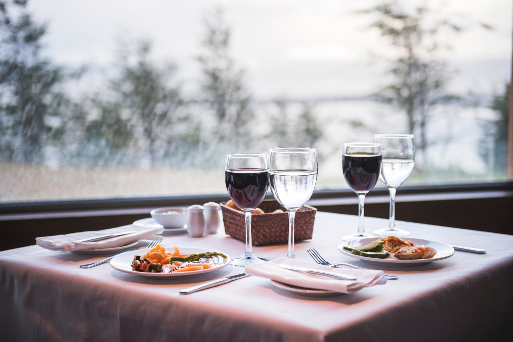 Elegant table at Ajax Tavern, Aspen, showcasing two glasses of wine alongside a selection of appetizing food.