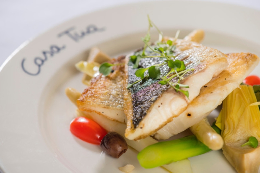 A gourmet dish of fish accompanied by vibrant vegetables, presented at  Casa Tua Aspen.