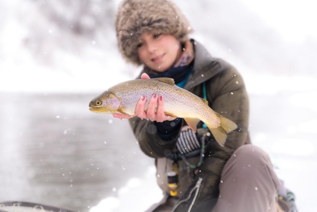 A woman proudly holds a fish in the snow, showcasing her catch from fly fishing on the Roaring Fork River.