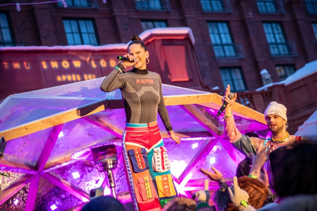 Aspen après-ski performance at The Snow Lodge, featuring a lively singer entertaining an enthusiastic crowd against a vibrant, wintery backdrop.