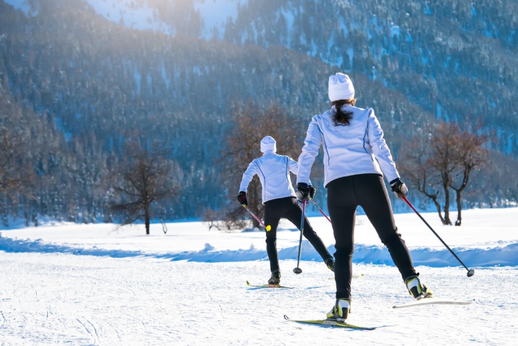 Two people enjoying cross country skiing in Aspen in January, gliding over a snow-covered trail with mountain scenery and winter trees in the background.