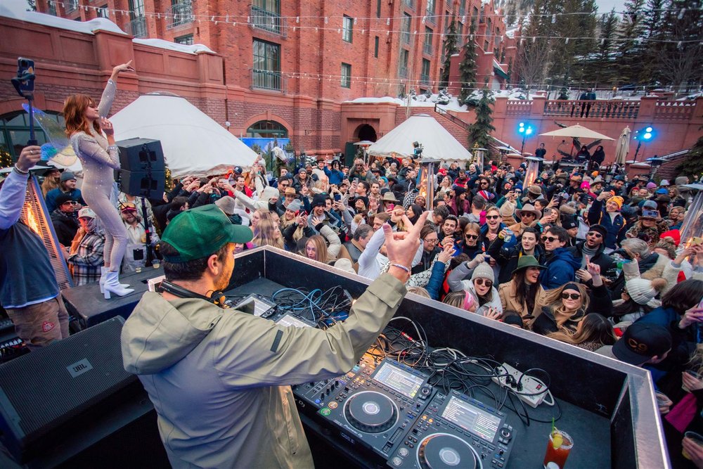 Crowd enjoying live music at Snow Lodge in Aspen in January, with a DJ performing and a singer on stage, creating a vibrant après-ski atmosphere.