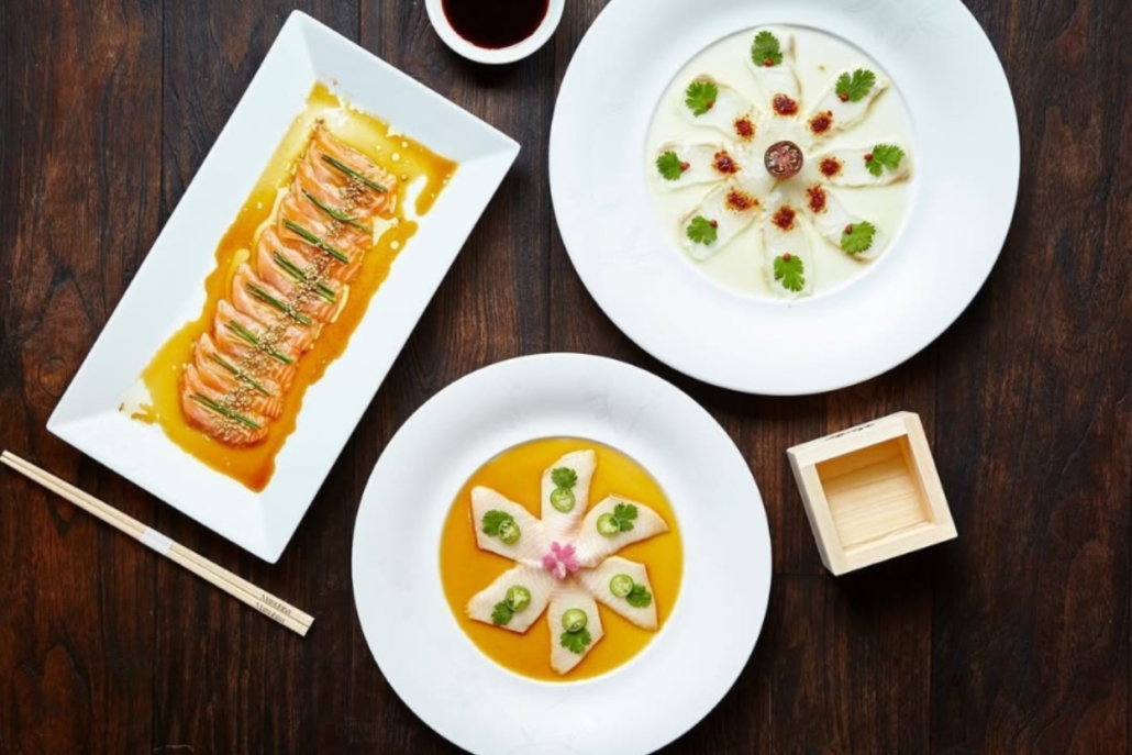 Three elegantly arranged plates of food on a wooden table, set for a dining experience at Matsuhisa during Aspen Bachelorette.