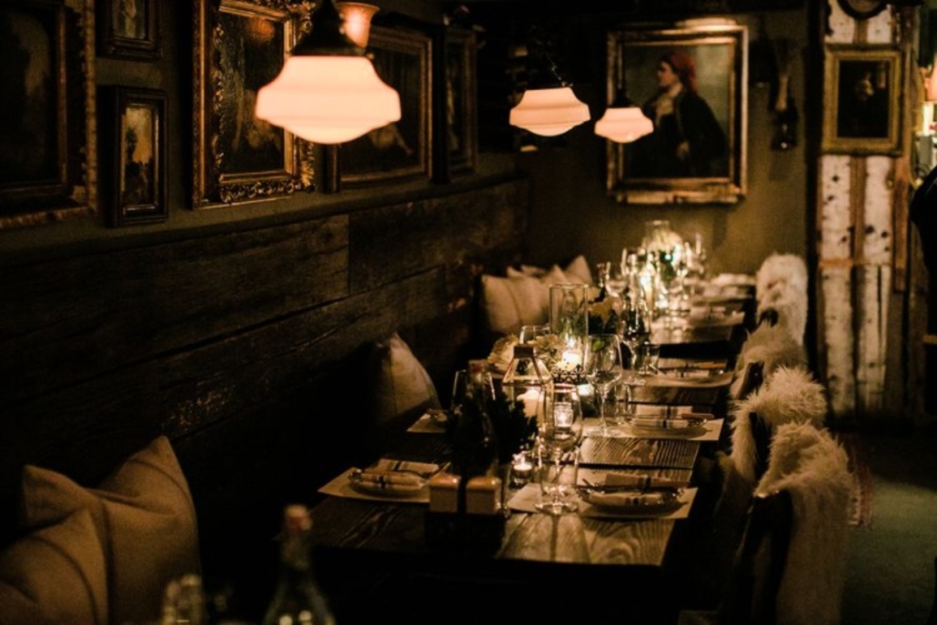 A long candlelit table with decorative paintings on the wall, set for the Aspen Bachelorette dinner at a French Alpine Bistro.