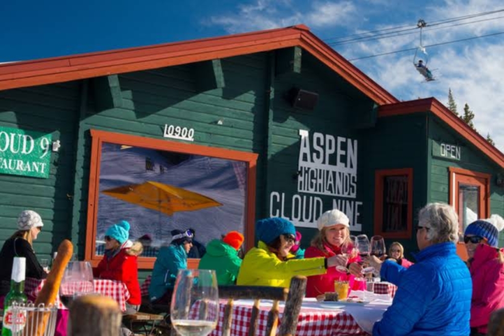 A lively outdoor scene with people at tables, toasting champagne for an Aspen bachelorette at Cloud 9 restaurant.