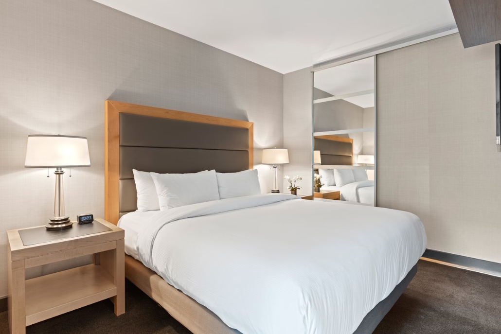 A bachelorette hotel room at The Little Nell, Aspen, with a comfortable bed, nightstand, and a decorative mirror.