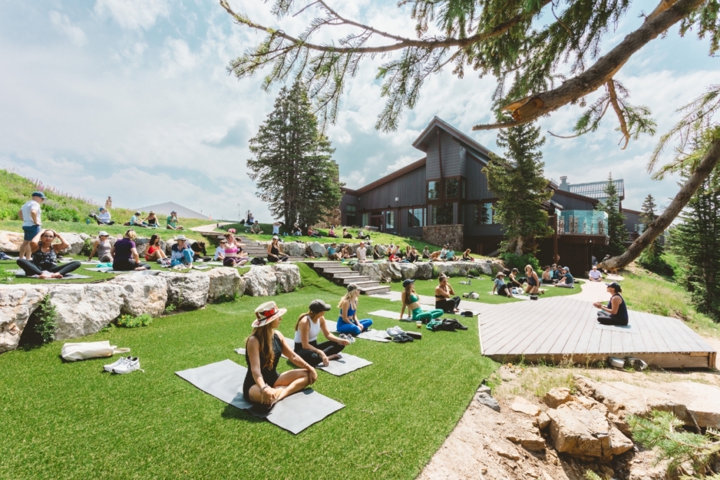 A group of people practicing yoga on grass with a mountain backdrop perfect for an Aspen activity during bachelorette party.