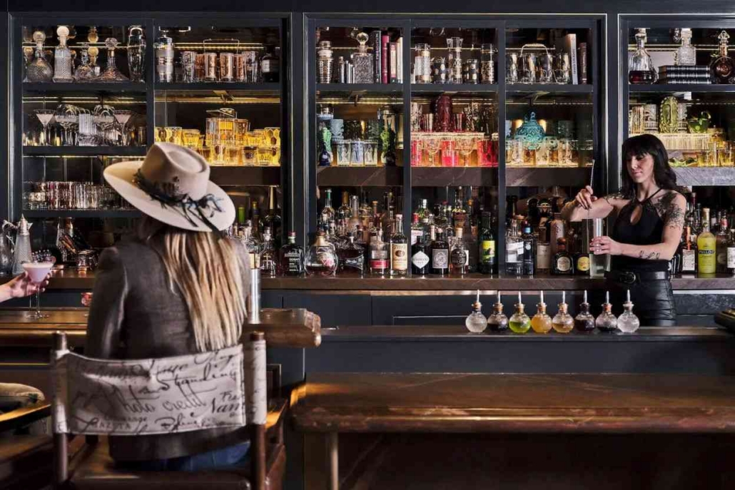 A woman stands behind the bar, serving drinks in a lively Aspen nightlife setting.
