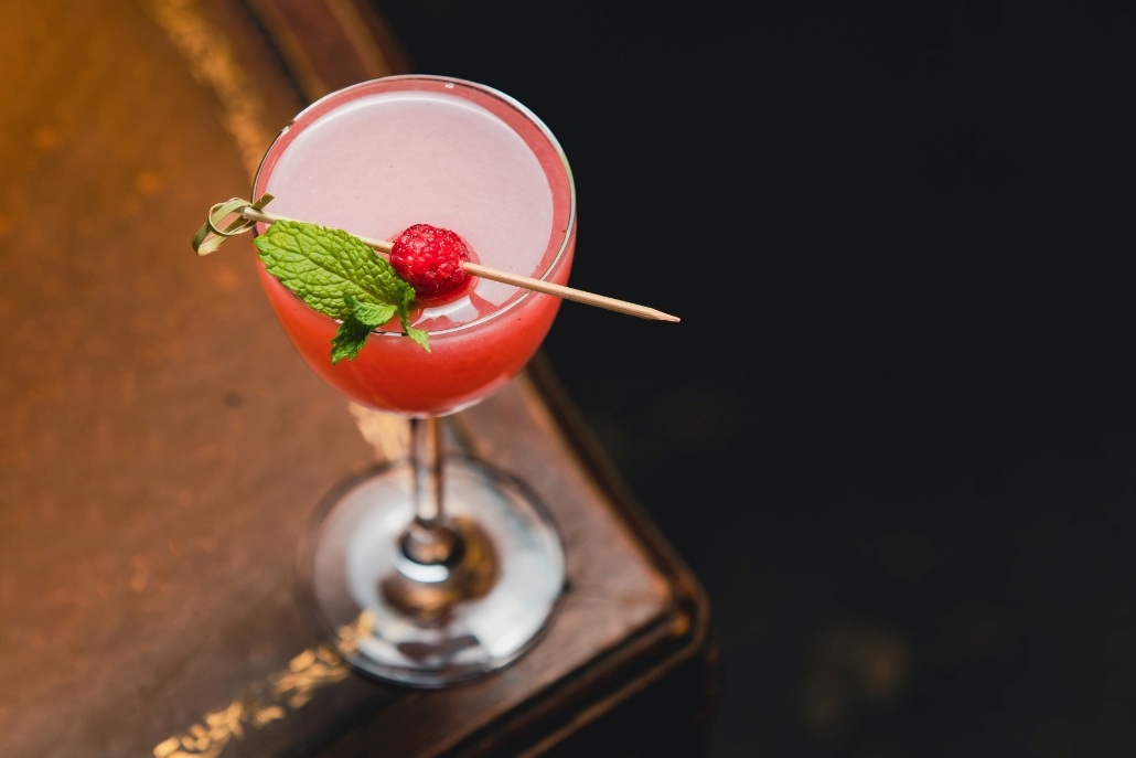 A refreshing cocktail with raspberry and mint sits on a wooden table, showcasing the ambiance of Hooch in Aspen Nightlife.