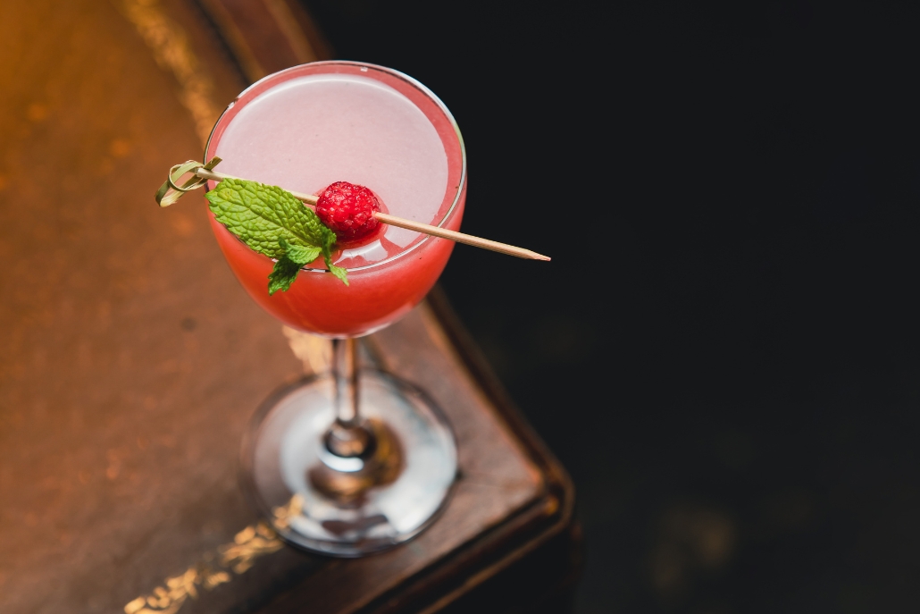 A refreshing cocktail with raspberry and mint sits on a wooden table, showcasing the ambiance of Hooch in Aspen Nightlife.