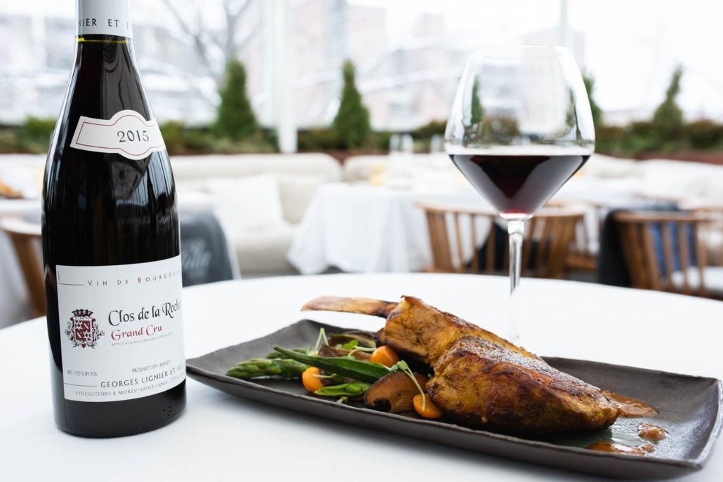 A table set with a glass of wine and a plate of food, highlighting the dining experience at Betula in Aspen's during summer.