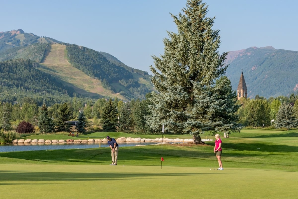 Two individuals playing golf on a lush course, with scenic mountains behind, highlighting Aspen's summer golf club.