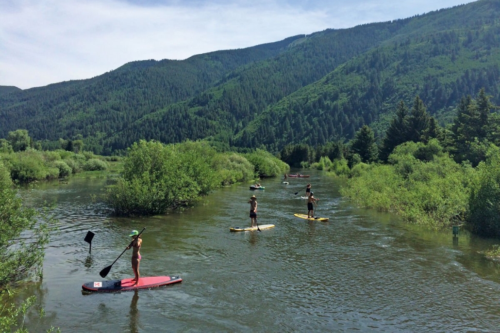 A group of people paddle boarding on a river during summer at North Star Preserve in Aspen.