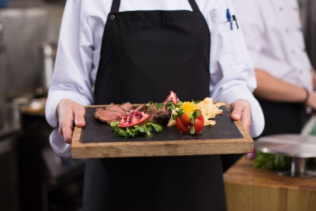 A chef holding a tray of elegantly arranged food at a private dinner event in Aspen, highlighting summer culinary experiences.