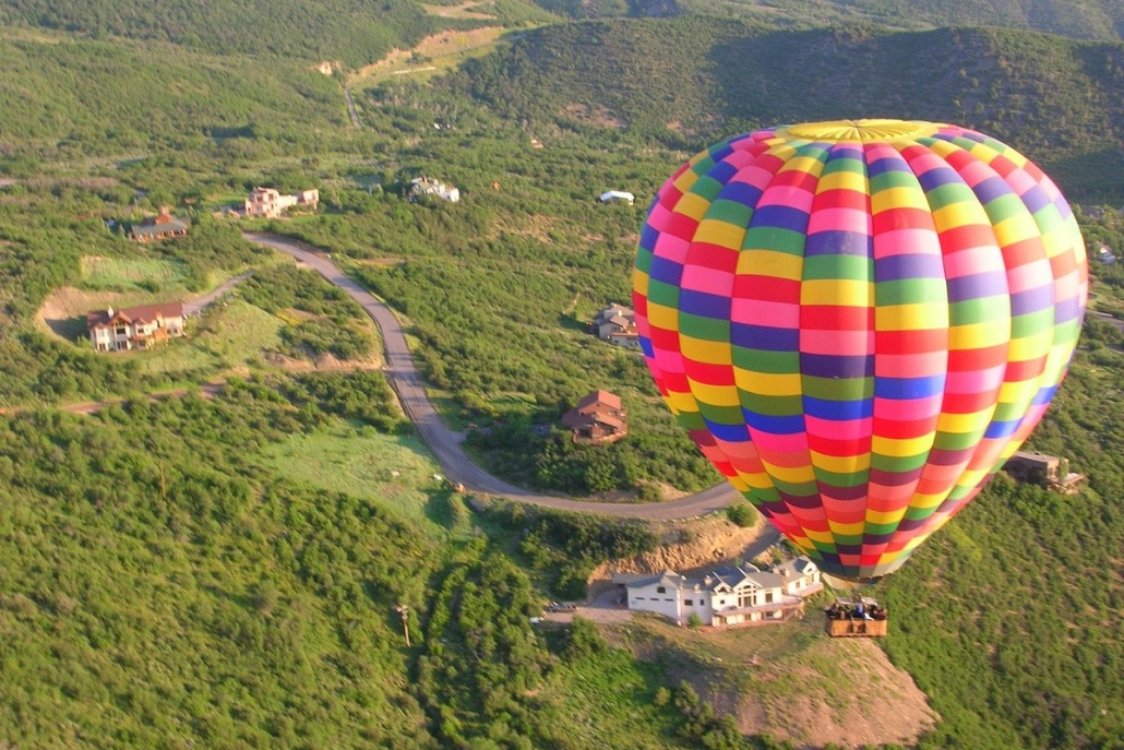 A vibrant hot air balloon glides above a verdant valley, highlighting a private summer ride in Aspen.