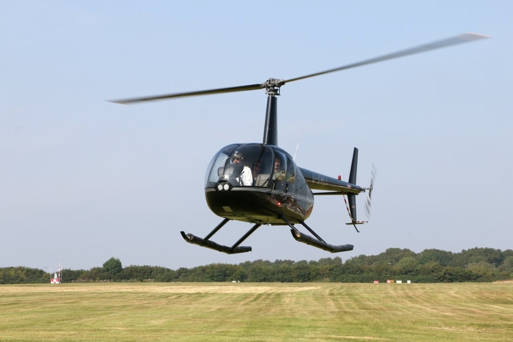 A helicopter soars above a green field and trees, highlighting summer helicopter tours available in Aspen.