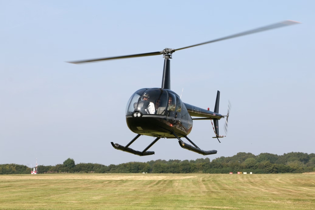 A helicopter soars above a green field and trees, highlighting summer helicopter tours available in Aspen.