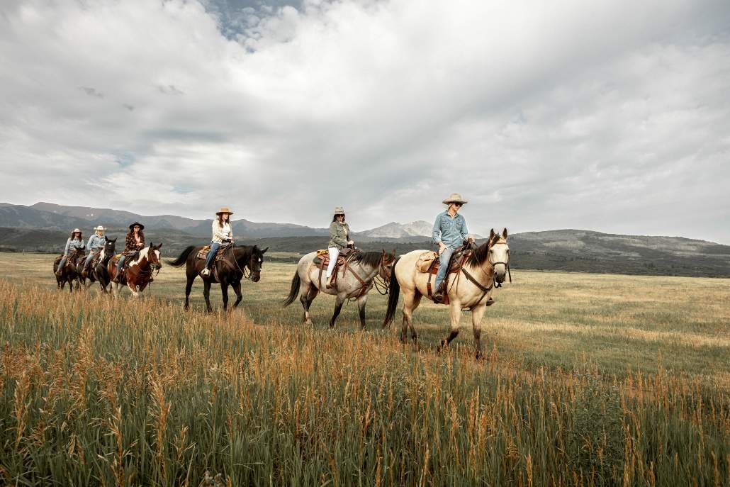 A group of people enjoy horseback riding in a grassy field, representing summer activities in Aspen.