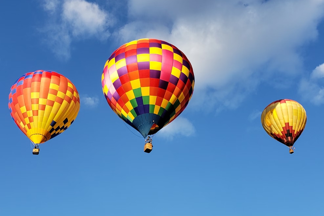 Three hot air balloons drifting in a sunny blue sky, representing summer experiences in Aspen.