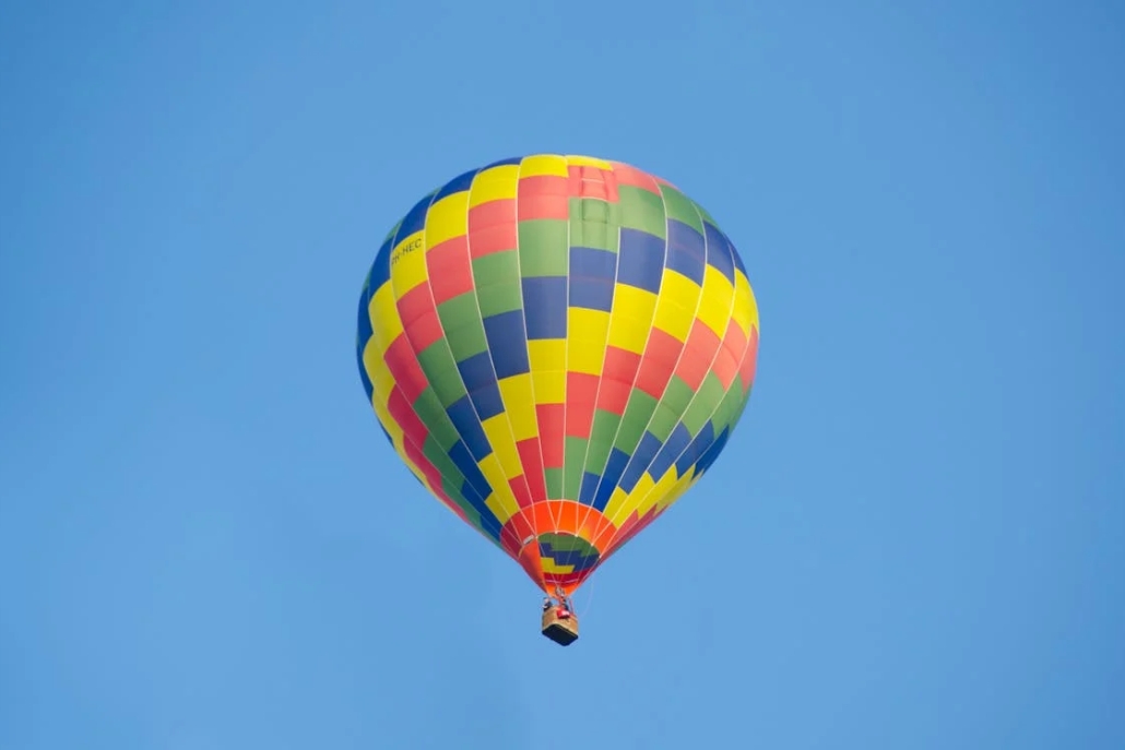 A striking hot air balloon floats in a sunny blue sky, showcasing Aspen's summer private hot air balloon ride offerings.