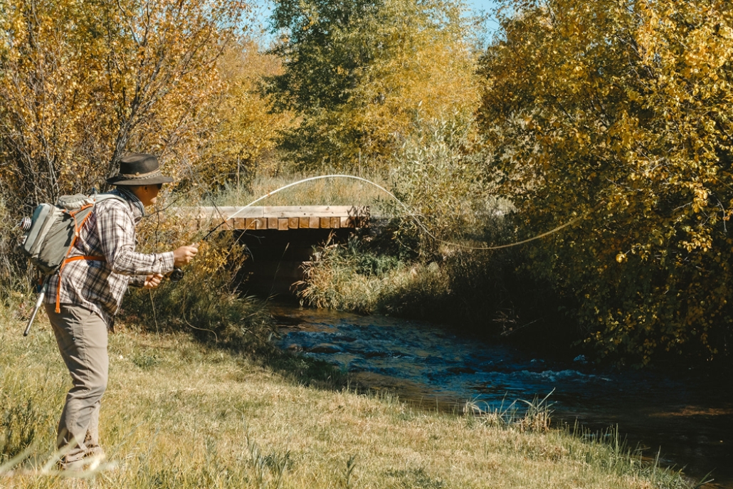 A man fly fishing in the Roaring Fork River surrounded by vibrant fall foliage in Aspen.